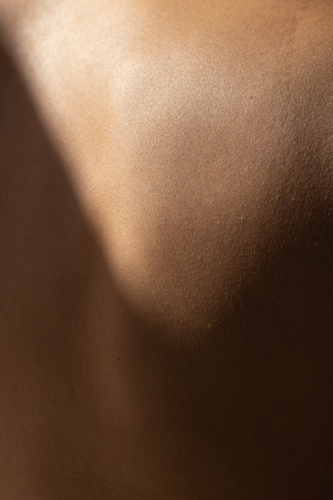 Close up sensual themed picture of lighter tone skin. A shadow appears across what seems to be the upper shoulder blade..  