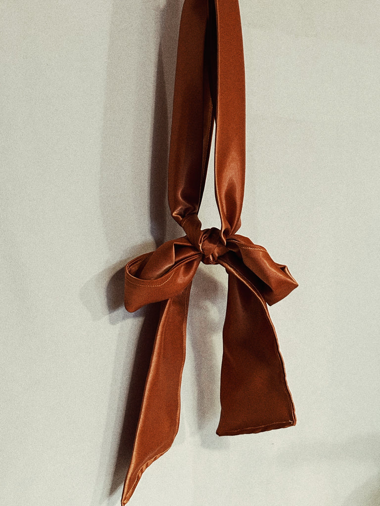 Explore the world of sensory play, kind and BDSM with this beginner friendly luxurious blindfold handcrafted in northern BC. Image shows bronze/copper satin blindfold hung in the centre of the image tied in a bow. 