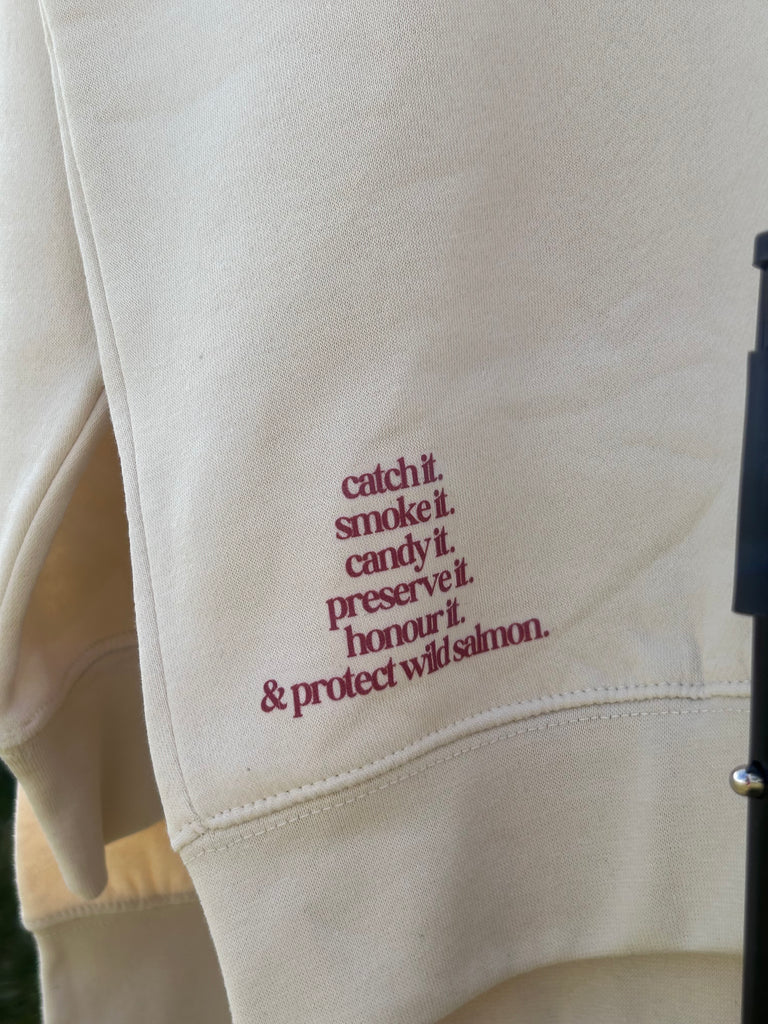 Cream crew neck sweater with multi indigenous salmon design and text in maroon with the saying ‘respect the logo’ in the centre. A nature, sustainable designed sweater with corner designs featuring ‘catch it, smoke it, candy it, preserve it, honour it, and protect wild salmon’ 