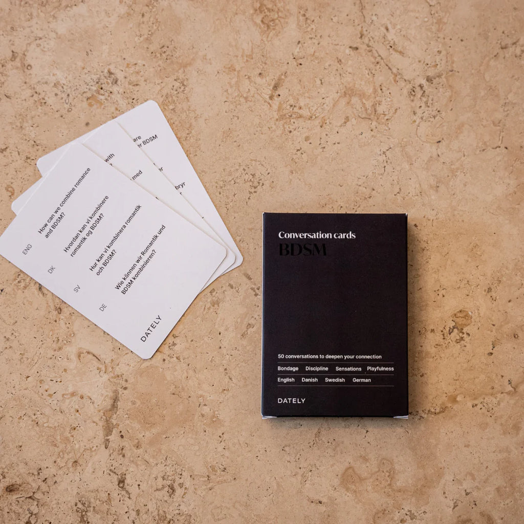 BDSM conversation cards for improving communication, understanding and connection in relationships. Helps to explore BDSM for beginners in a safe, open way. Cards displayed on marble table featuring 52 prompts on power dynamics, BDSM, intimacy and sensuality. 