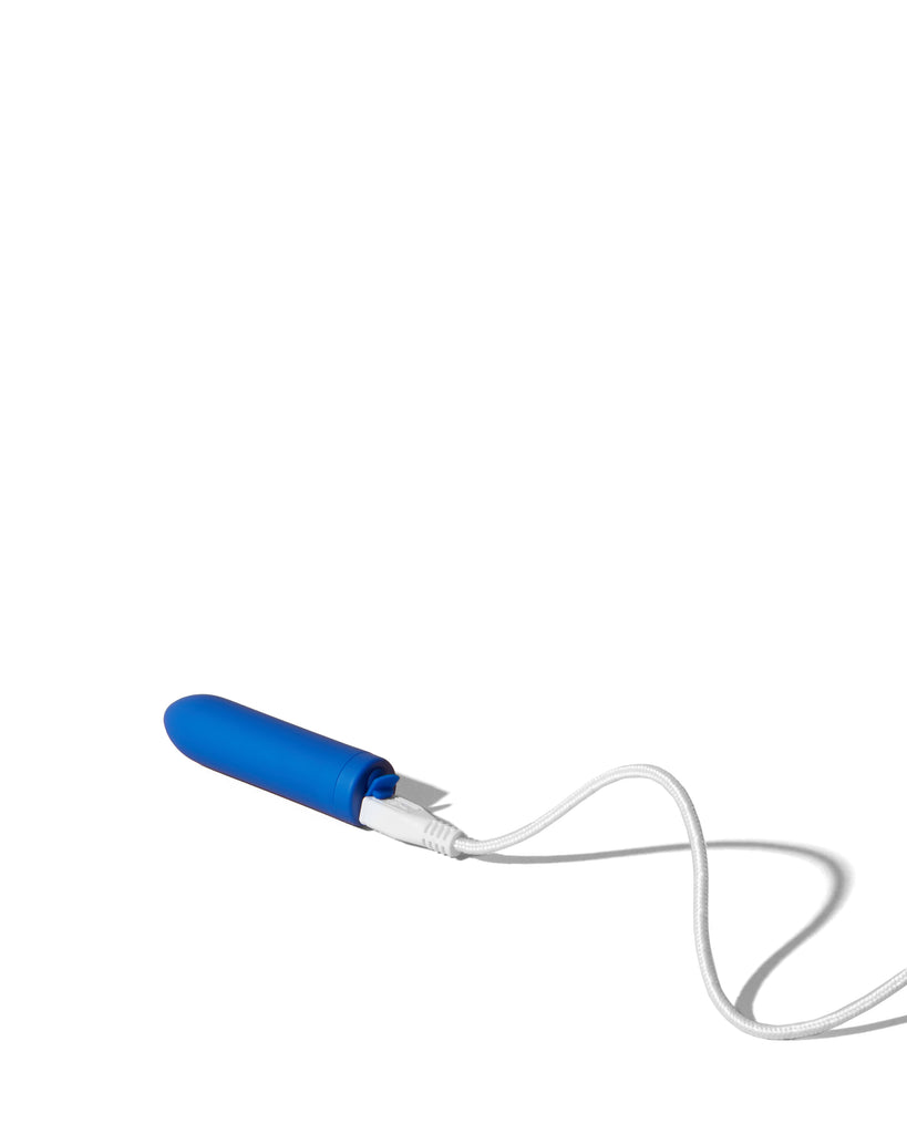Blue Zee bullet vibe by Dame displayed laying horizontally with white charging cable attached on solid white background.