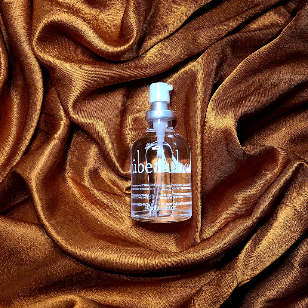 Clear glass bottle of Uberlube in 50ml size laid on copper satin background.