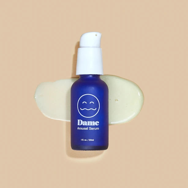 Dark blue bottle of Dames arousal serum in 1oz/30ml laid infront of sample of serum spread in front of solid beige background. 