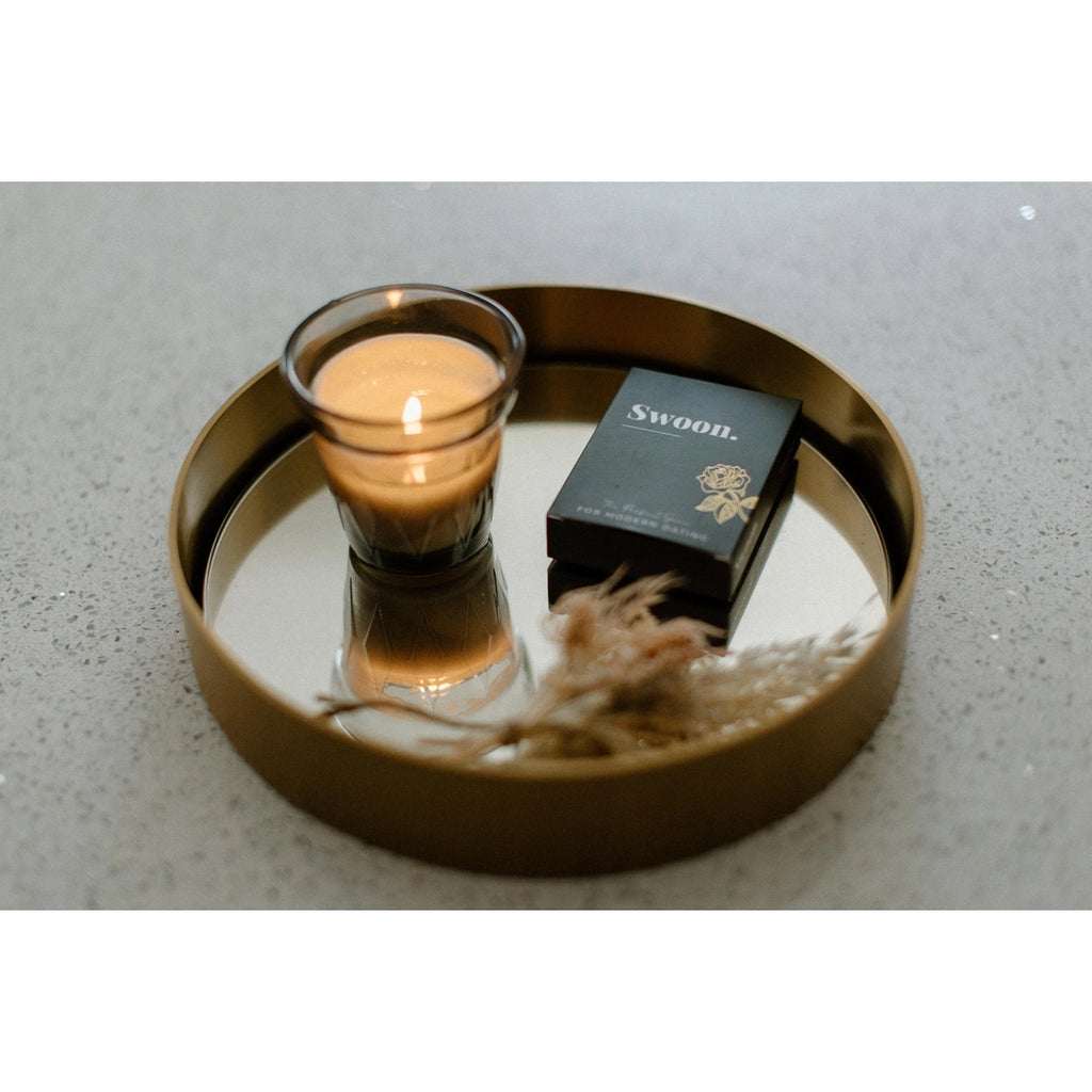 Romantic scene with circular trey on cement holding decorative grass, candle. Displaying black box of swoon deck of cards. 