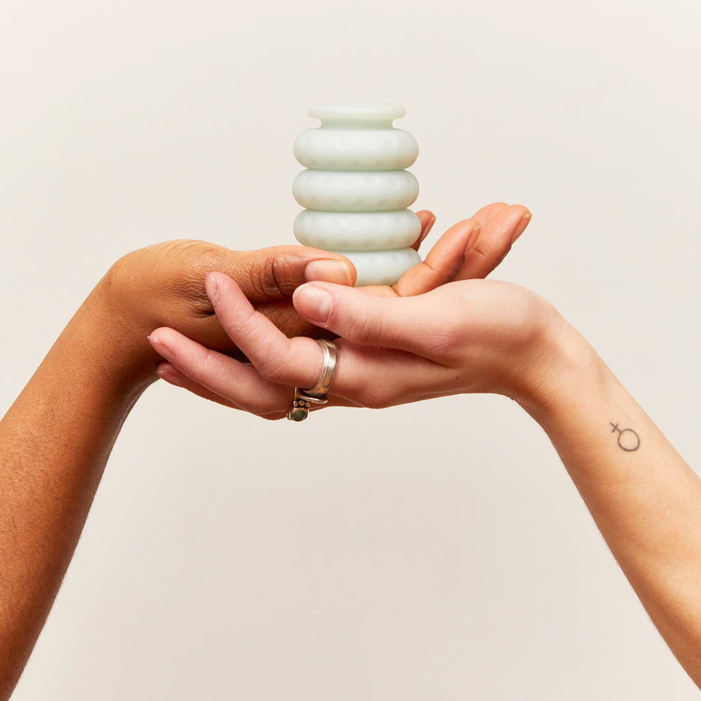 Oh Nut brand silicon intimate wellness buffer in the colour jade being held in two individuals hands to display the product against off white background