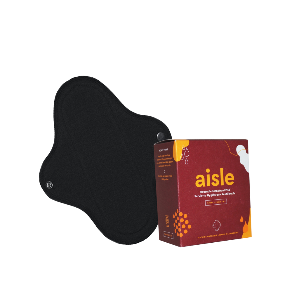 Red decorated box of Aisle mini reusable menstrual pad in front of black cotton pad with snap enclosures in front of white background.