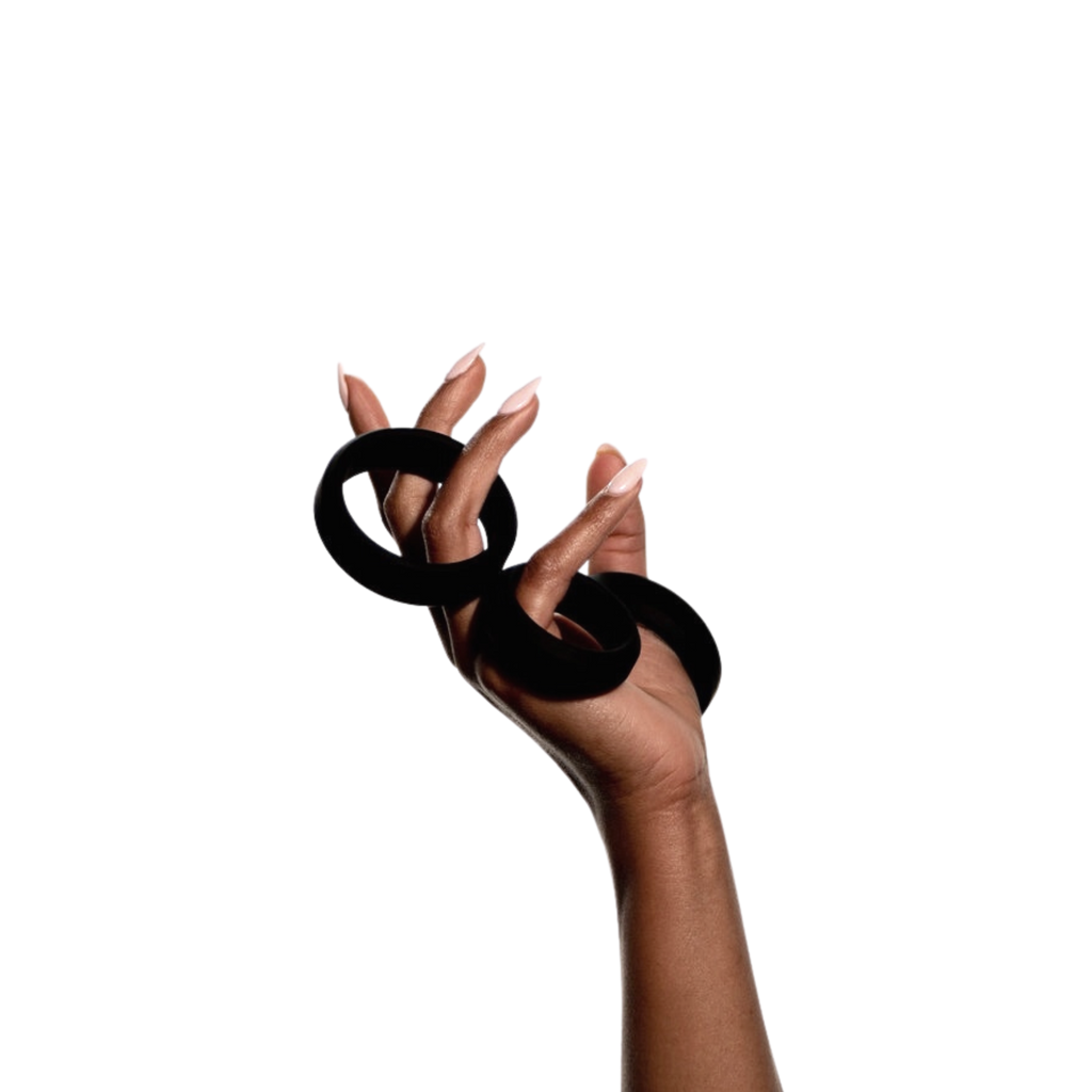 Feminine hand vertically holding three black multi-sized silicon cock rings by Wednesday Co against on solid white background.