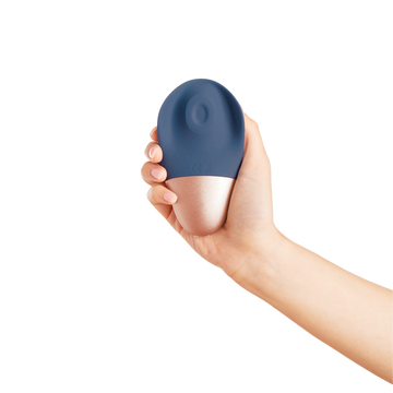 Feminine hand holding Deia Arouser clitoral stimulator being held in front of solid white background background.
