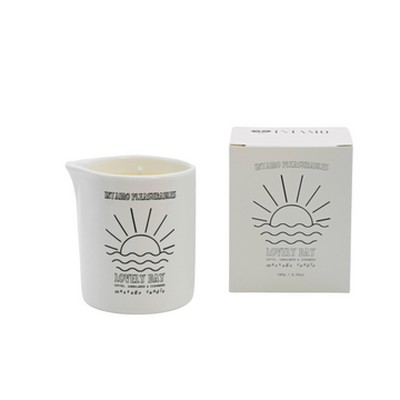 Lovely day massage candle by Intamo product and box placed to the right displayed on solid white background. Both items feature sunset illustration and Intamo logo. 