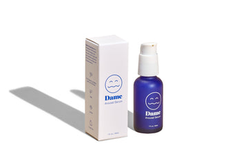 Dark blue bottle of Dames arousal serum in 1oz/30ml standing vertically with product box to the left on solid white background. 