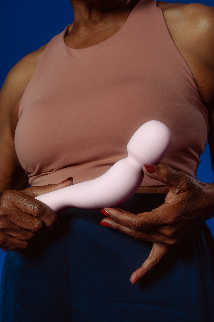 women holding Dames silicon Com wand vibrator in colour quartz in front of mid section of body against dark blue background.