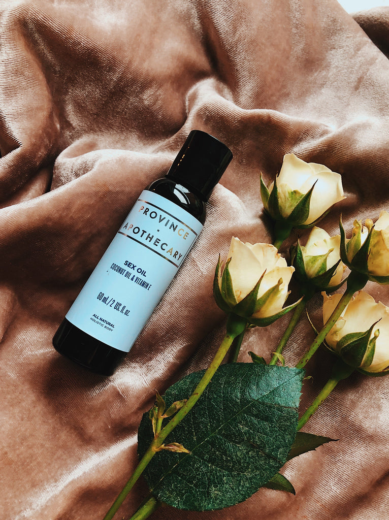Province Apothecary's sex oil in 60ml bottle displayed in a romantically decorated scene featuring product bottle laying on dusty pink velvet fabric with yellow roses laid beside.
